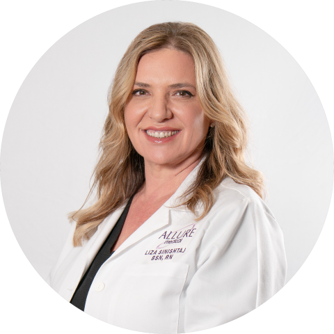 A woman with wavy blonde hair wearing a white medical coat, smiling at the camera against a plain light background.
