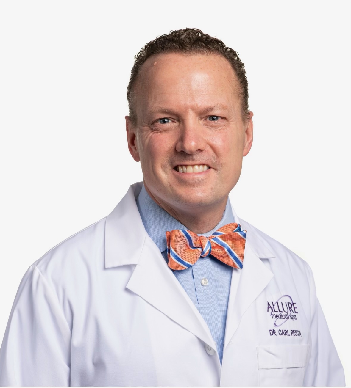 A man in a white lab coat with a badge labeled "Dr. Carl Pestl" from Allure Medspa is smiling. He is wearing an orange and blue striped bow tie and a light blue shirt.