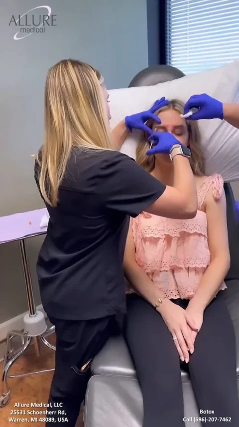 A woman receives a Botox injection on her forehead while seated in a medical office. A practitioner wearing gloves administers the treatment.