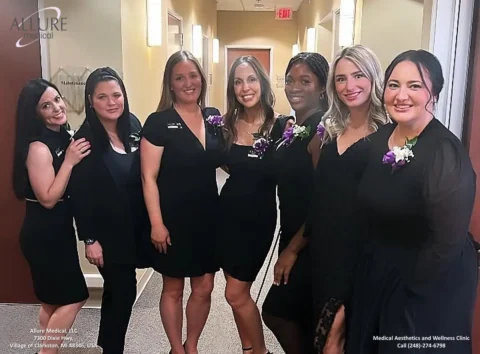 Six women wearing black dresses stand together in a hallway, smiling at the camera.