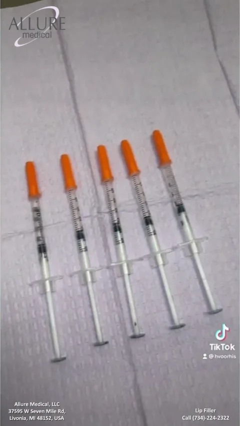 Five syringes with orange caps are lined up on a white surface. The background includes contact information for Allure Medical, LLC.