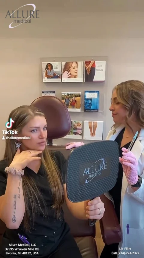 A woman is sitting in a medical office, holding a mirror with "Allure Medical" on it, while a healthcare professional in a white coat and gloves stands beside her.