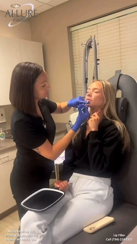 A woman reclines in a chair while a healthcare professional administers a lip filler injection. A sign in the background reads "Allure Medical." Contact information is visible at the bottom right.