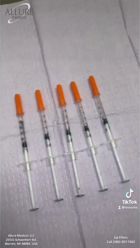 Six syringes with orange caps are laid out in a row on a white medical pad. The image includes contact information for Allure Medical, LLC in Warren, MI, and a TikTok username and phone number.