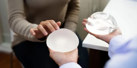 A person in a beige top examines two silicone implants held by another individual.