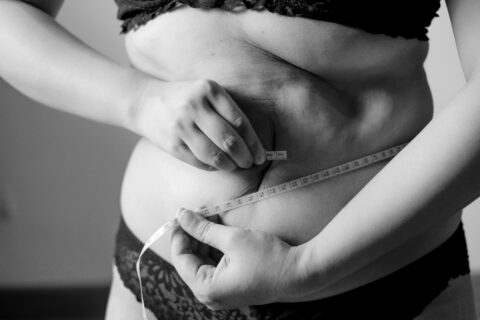 A person in underwear measures their waist with a measuring tape.