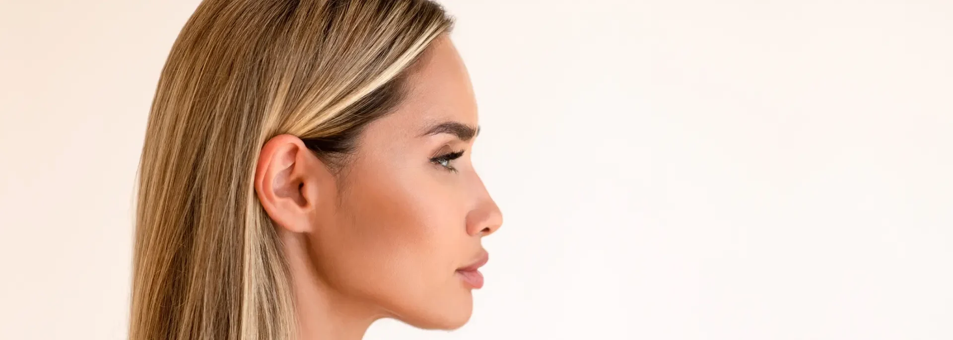 Profile view of a woman with straight, blonde hair and clear skin against a plain, light background.