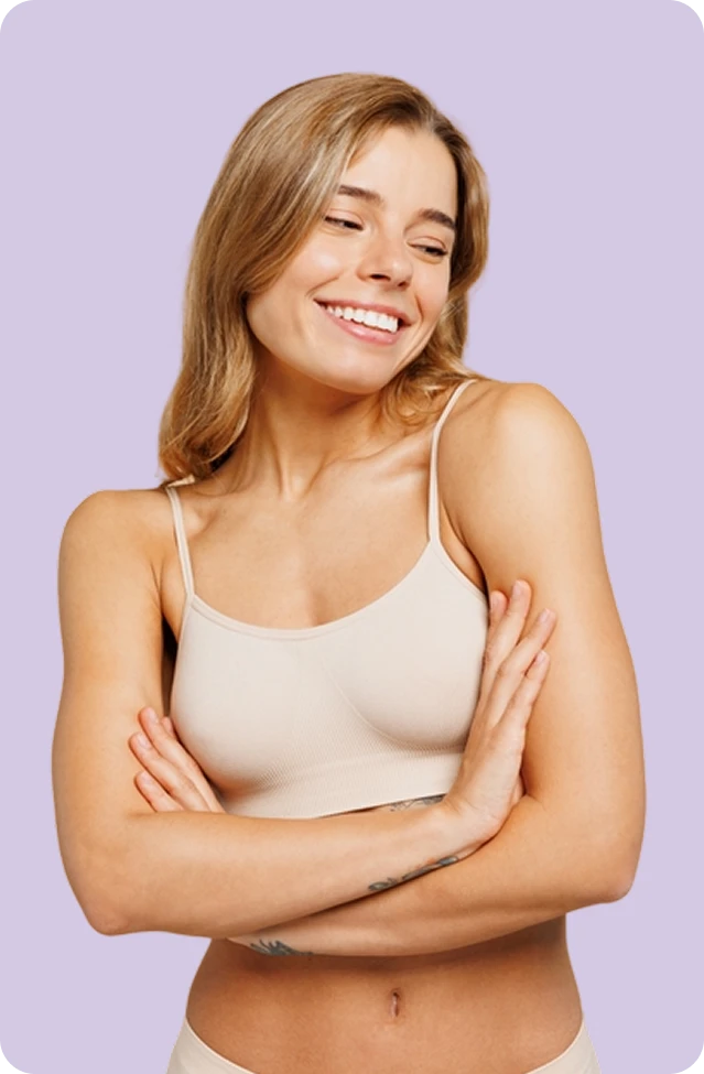 A woman with long blonde hair wearing a beige camisole stands with her arms crossed, smiling and looking to the side against a light purple background.