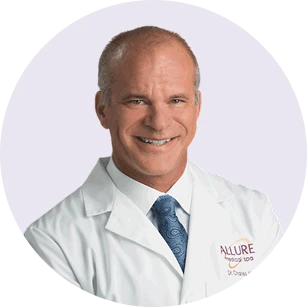 Smiling middle-aged man in a white lab coat with "Allure Medical Spa" logo, wearing a blue tie, posed against a light background.