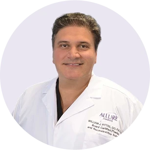 A man in a white medical coat with "Allure" and his name embroidered on it, smiling at the camera against a light background.