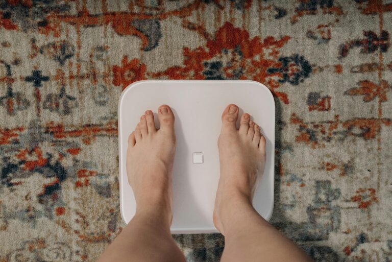 A person standing barefoot on a white digital scale placed on a patterned rug.